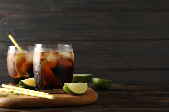 Glasses with ice cola, lime slices and tubules on wooden background