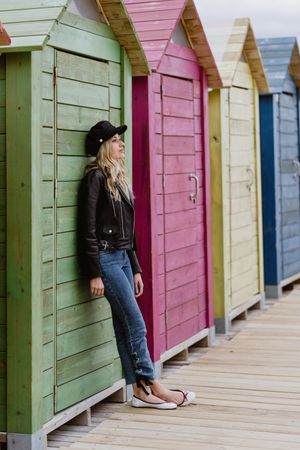 Stylish woman smiling and leaning on bright wooden cabins on beach