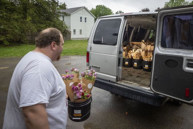 Copake, New York - May 19, 2022: Man walking towards back of delivery truck with bucket of flowers