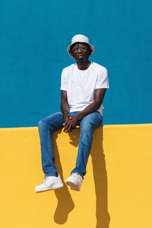 Happy Black man sitting on colorful wall
