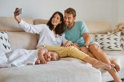 Mother and father taking selfie on phone near sleeping daughter