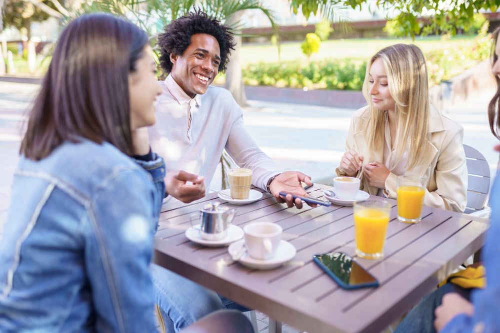 Multi-ethnic friends smiling over coffee and juice at outside table