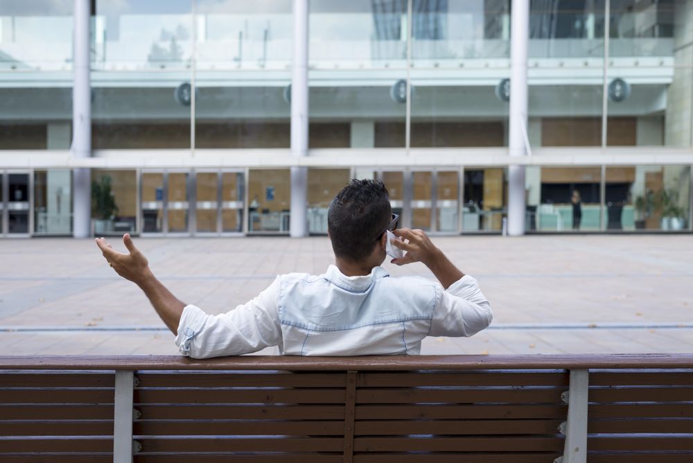 Back of male sitting on bench having conversation on phone