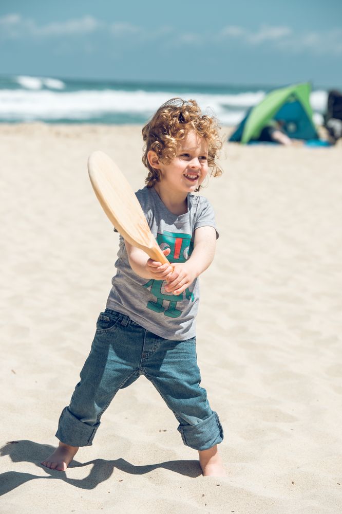 Content boy playing with racket on beach