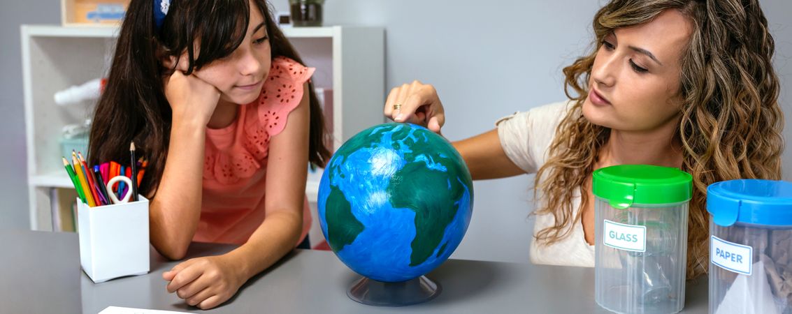 Female teacher giving ecology lesson with handmade globe world to girl student
