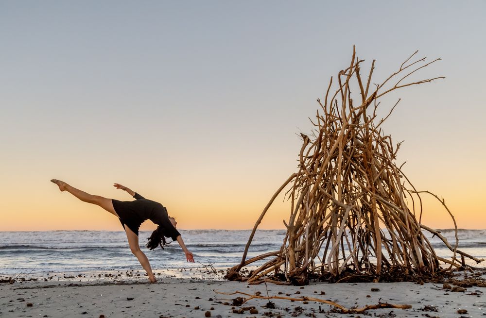 Young woman dancing on shore near water and wooden twigs placed for campfire