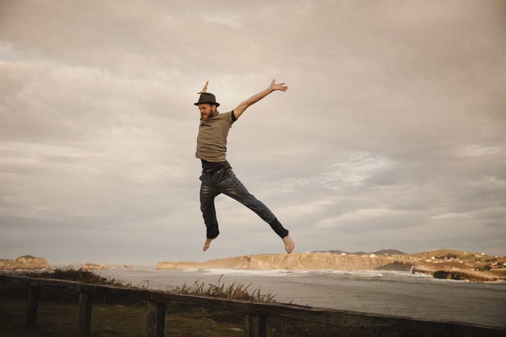 Young man in hats having fun on seat on coast near waving sea and cloudy sky