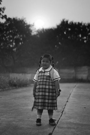 Grayscale photo of young girl in school uniform standing outdoor in grayscale