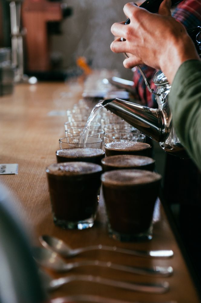 Close up cropped shot of hands pouring hot water into glasses for drinking coffee