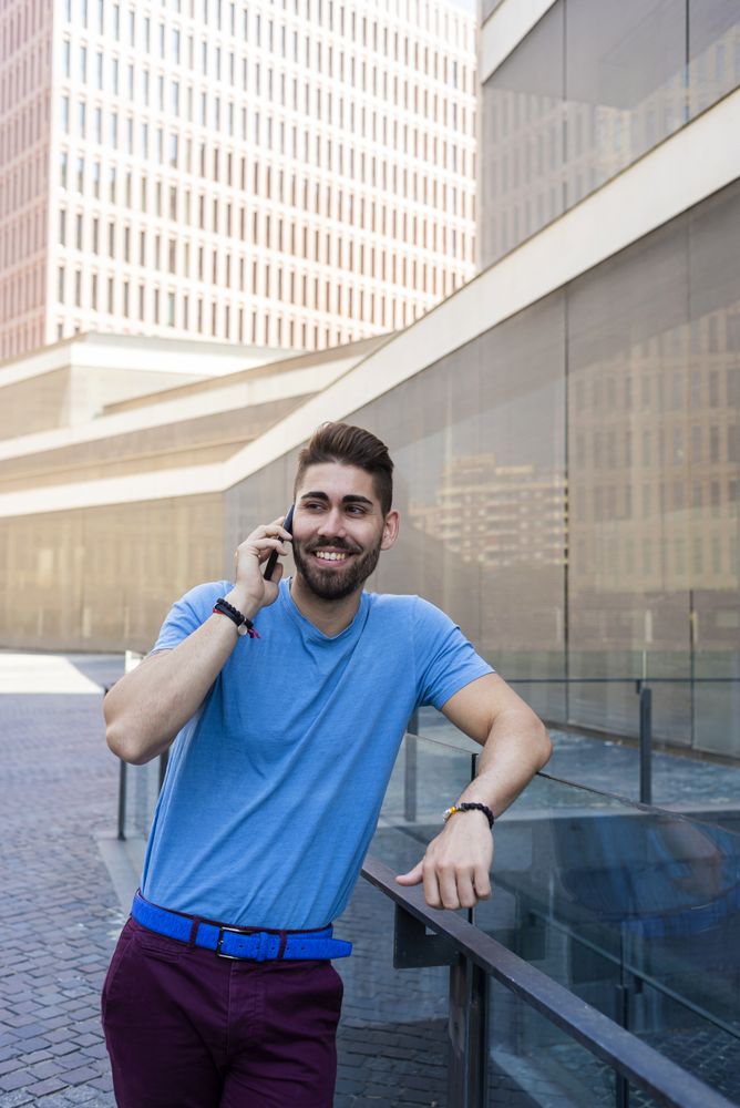 Man leaning on glass railing outside having conversation on mobile phone