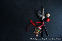 Dark knife and fork on dark background tied with bright red ribbon and gingerbread decoration 0yk2O4