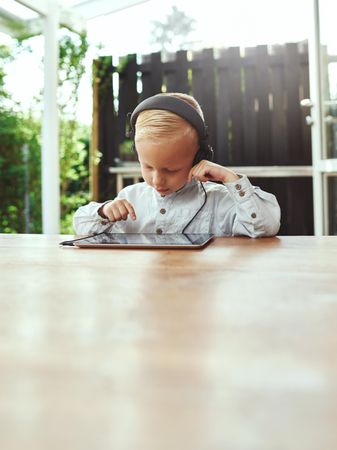 Smiling blond boy using headphones listening to something on digital tablet, copy space