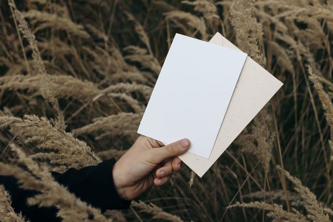 Kids hand holding blank greeting card, invitation mockup with craft envelope outdoor