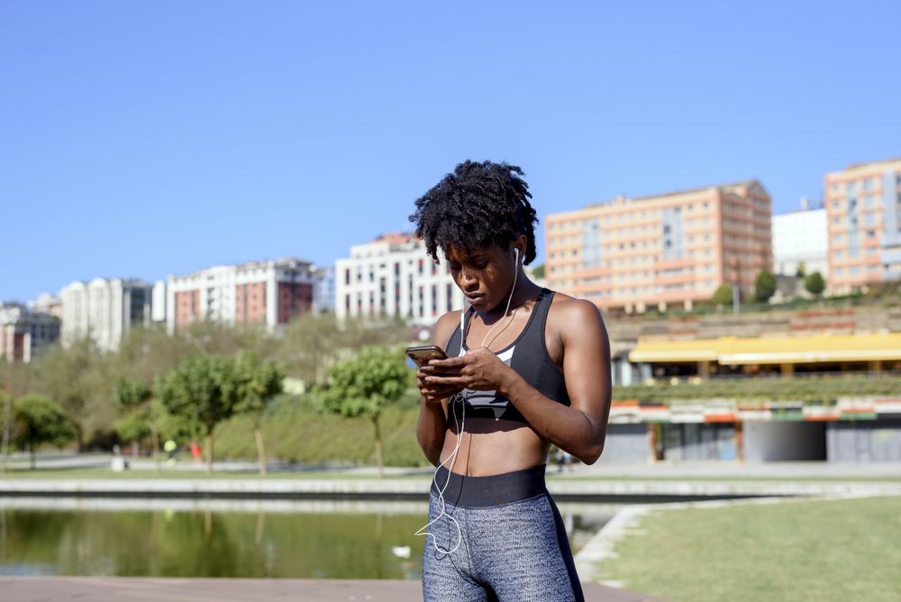 Cheerful Black sportswoman listening to music on smartphone