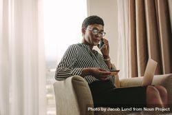 Woman sitting in armchair with laptop and credit card talking over mobile phone 4BmnP5