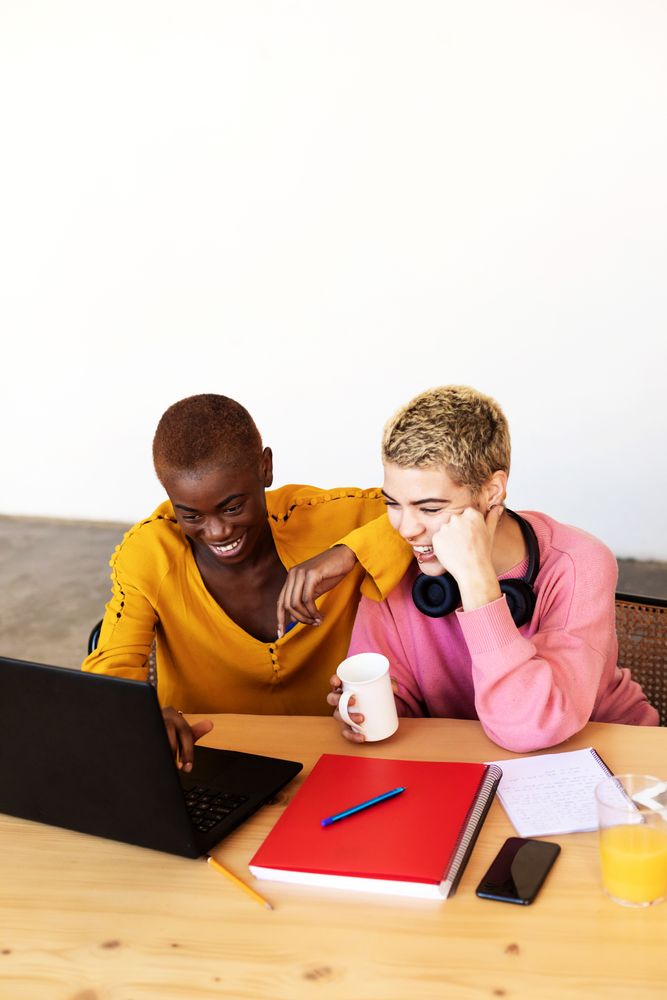 Laughing female friends using laptop at breakfast
