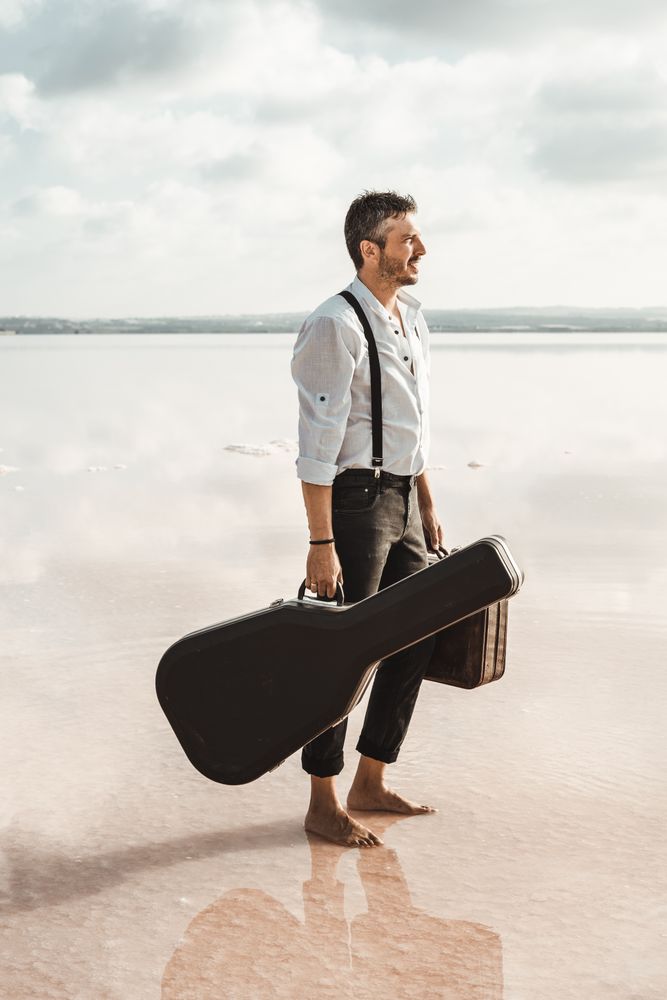 Focused stylish man with suitcase and guitar gig bag on seaside