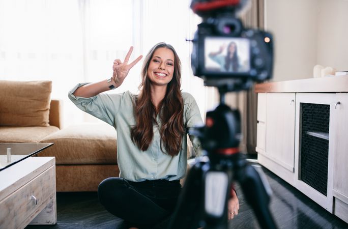 Smiling woman showing victory or peace sign on camera