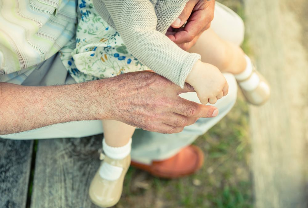 Baby girl holding finger of older man's hand