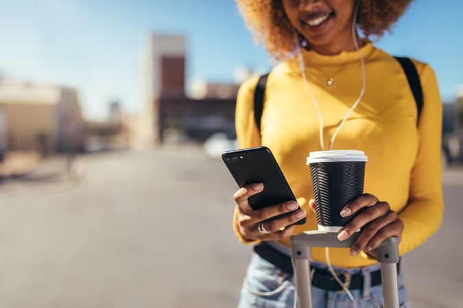 Close up of woman traveller holding coffee cup while looking at smart phone
