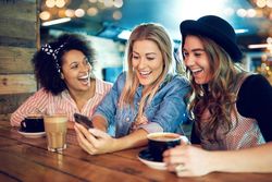 Girlfriends sharing a laugh over a cell phone at a coffee shop