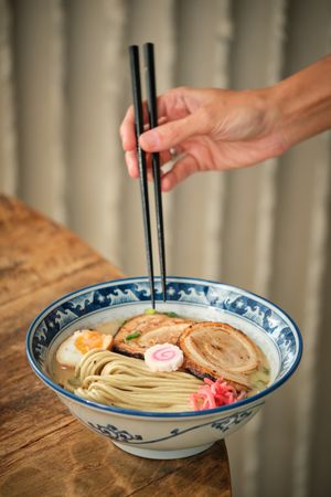 Crop person eating ramen noodles with chopsticks