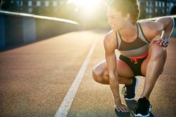 Muscular woman crouching down on sunny bridge