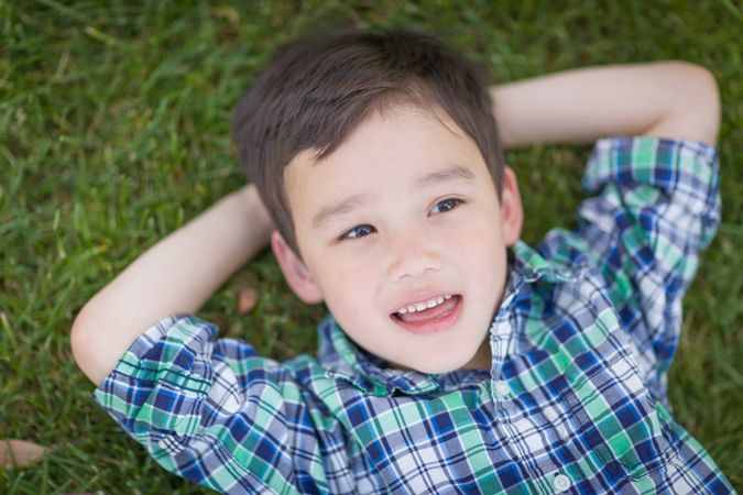 Boy Relaxing On His Back Outside On The Grass