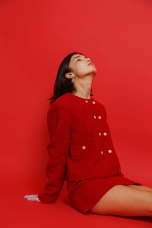 Woman in red skirt suit sitting against red background
