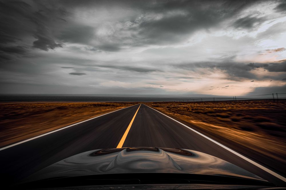 Dark car on road under cloudy sky
