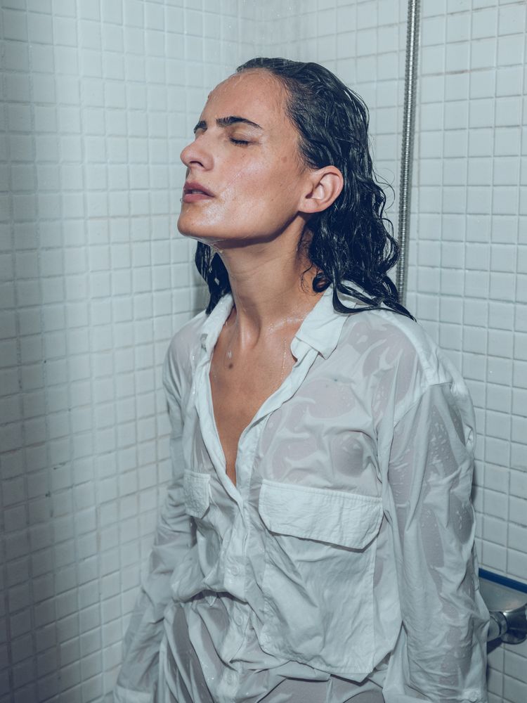 Confident woman in wet shirt under water in shower cabin