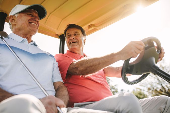 Low angle shot of two older men driving in a golf cart
