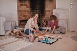 Positive woman teaching boy to create picture with paints