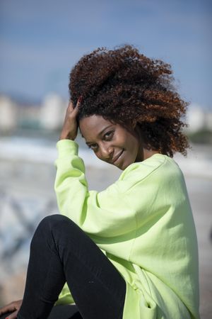 Vertical portrait of female with curly hair in bright green shirt sitting outside