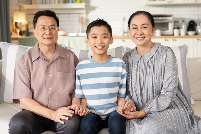 Happy Asian grandson and grandparents relax sitting on couch in the living room