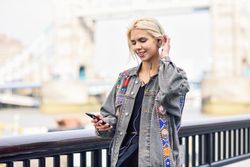 Happy blonde woman listening to music on phone along river walk
