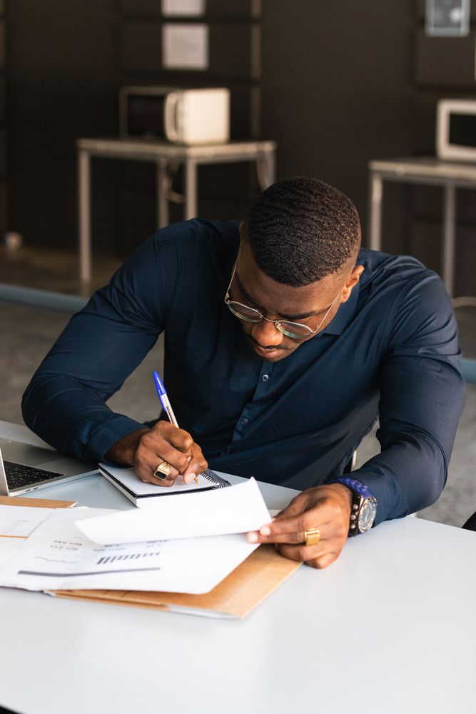 Black male writing in notepad near laptop in office