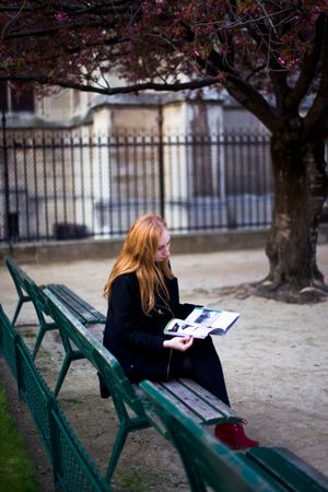 Woman sitting on green bench reading book in the park
