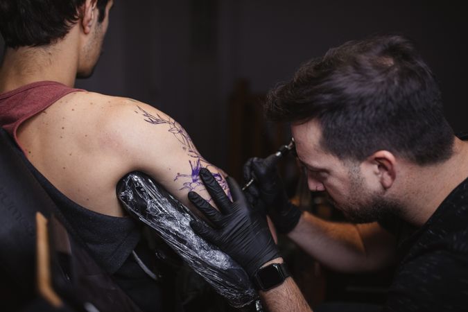 Master doing tattoo on forearm of male customer