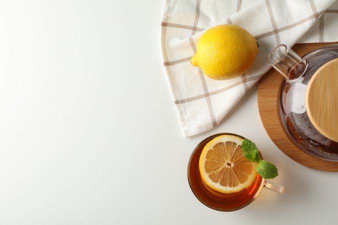 Cup of tea, mint, lemon, tea pot and towel on plain background, copy space