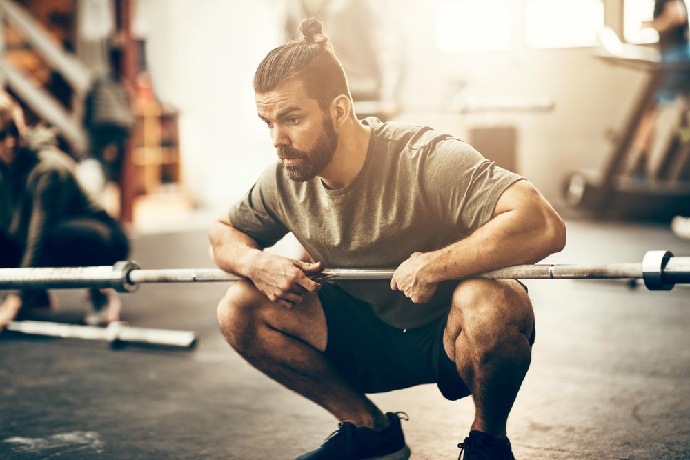 Focused man holding barbell on knees on floor