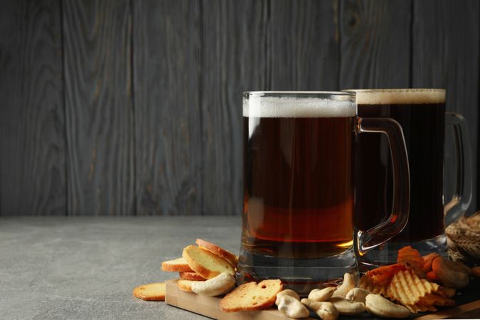 Beer and snacks on gray table against wooden background
