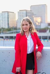 Happy woman in red coat standing on top of building with view of city behind her
