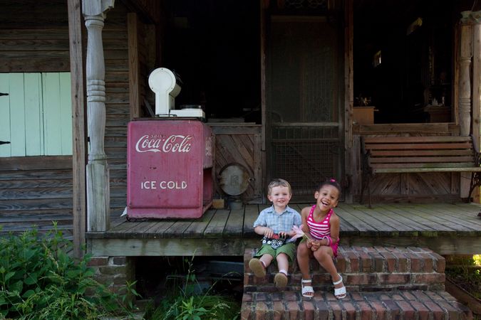 Two young children sit on steps of rustic cabin front porch in rural Alabama