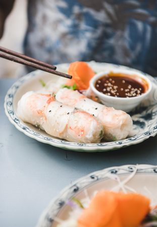 Chopsticks held above spring rolls, with dipping sauce