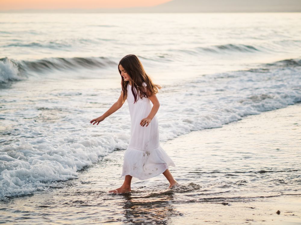 Adorable girl walking and playing on seaside at sunset