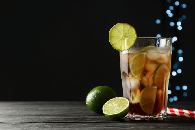 Glass of cold cola with citrus and ice on wooden table against dark background