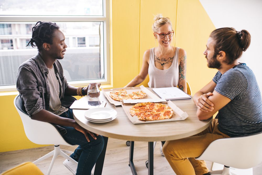 Three colleagues having an enjoyable lunch break with pizza at the office