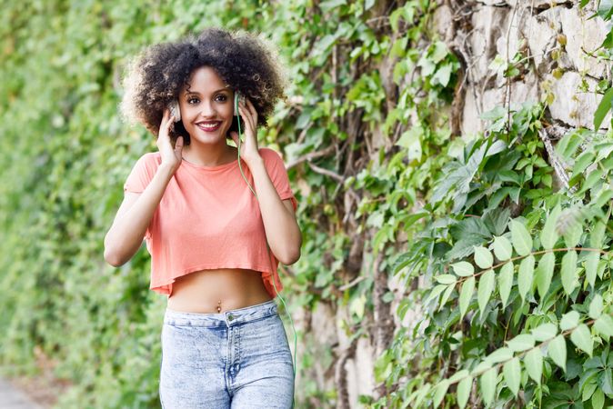 Smiling woman walking next to wall with vines wearing orange t-shirt and blue jeans