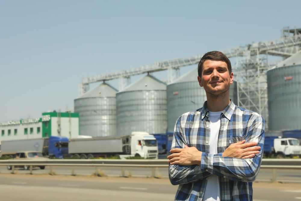 Young man against grain silos. Agriculture business